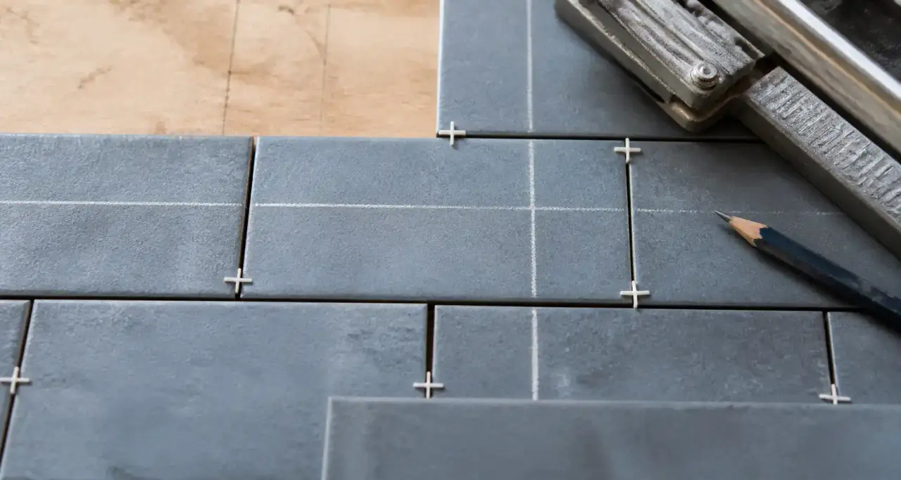Détail d'un calepinage de carrelage gris-bleu ardoise en cours de pose, joints et cales visibles